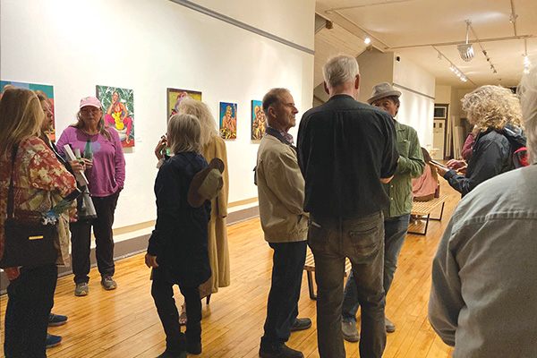 People are gathered at a gallery talking.