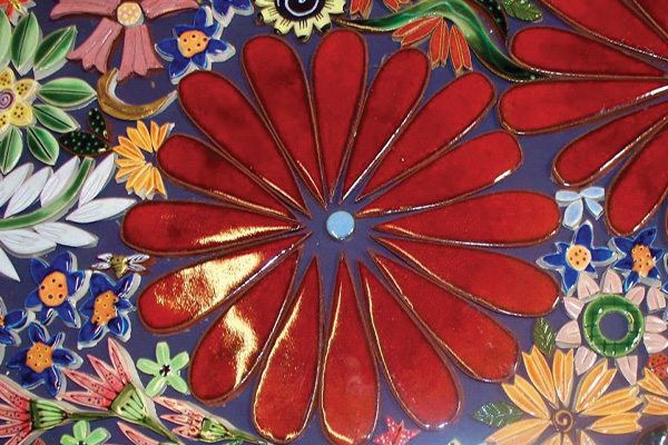 An extreme close up of a Spanish tile with a bright red flower in the middle.