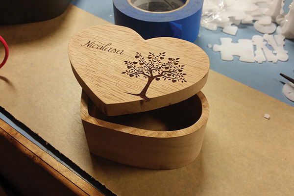 A wooden box with a tree engraved on it sits on a table with the lid askew.